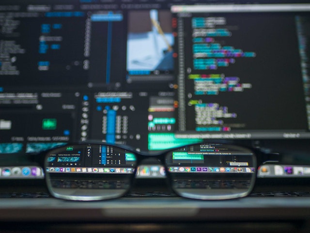 A photo of eye glasses in front of monitors showing code